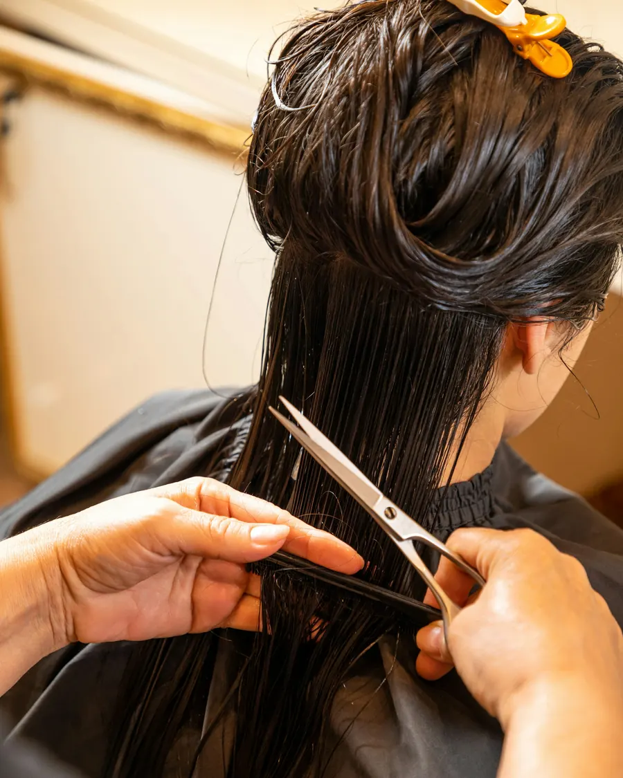 Hände schneiden langes, nasses, dunkles Haar mit der Schere